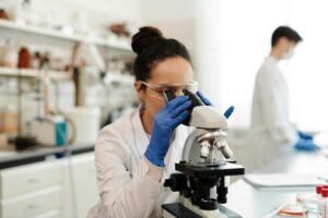 pexels-photo-4033304-4033304 A female scientist in protective gear examines samples through a microscope in a laboratory setting.