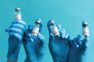 Hands in blue gloves holding COVID-19 vaccine vials against a blue background.
