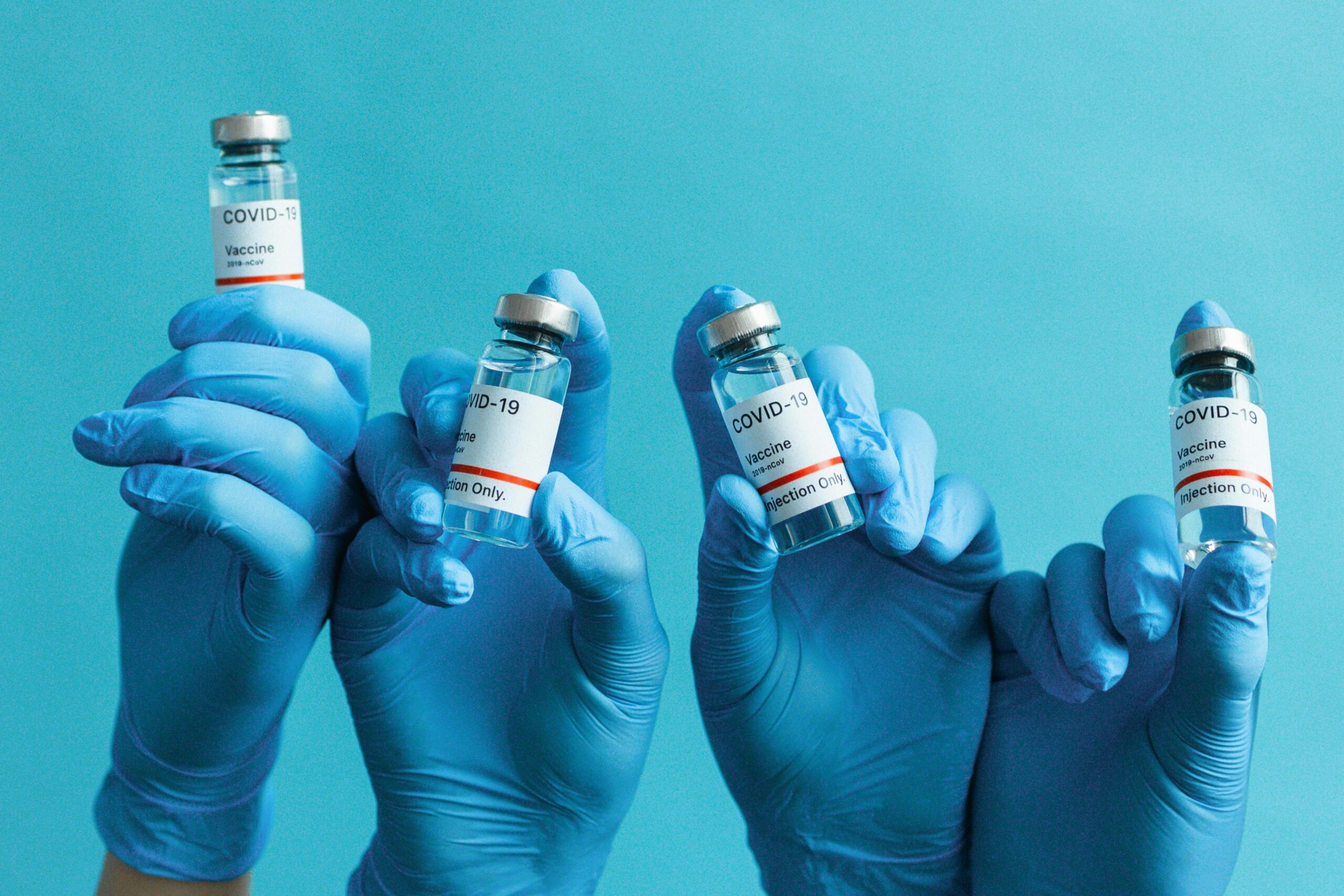 Hands in blue gloves holding COVID-19 vaccine vials against a blue background.