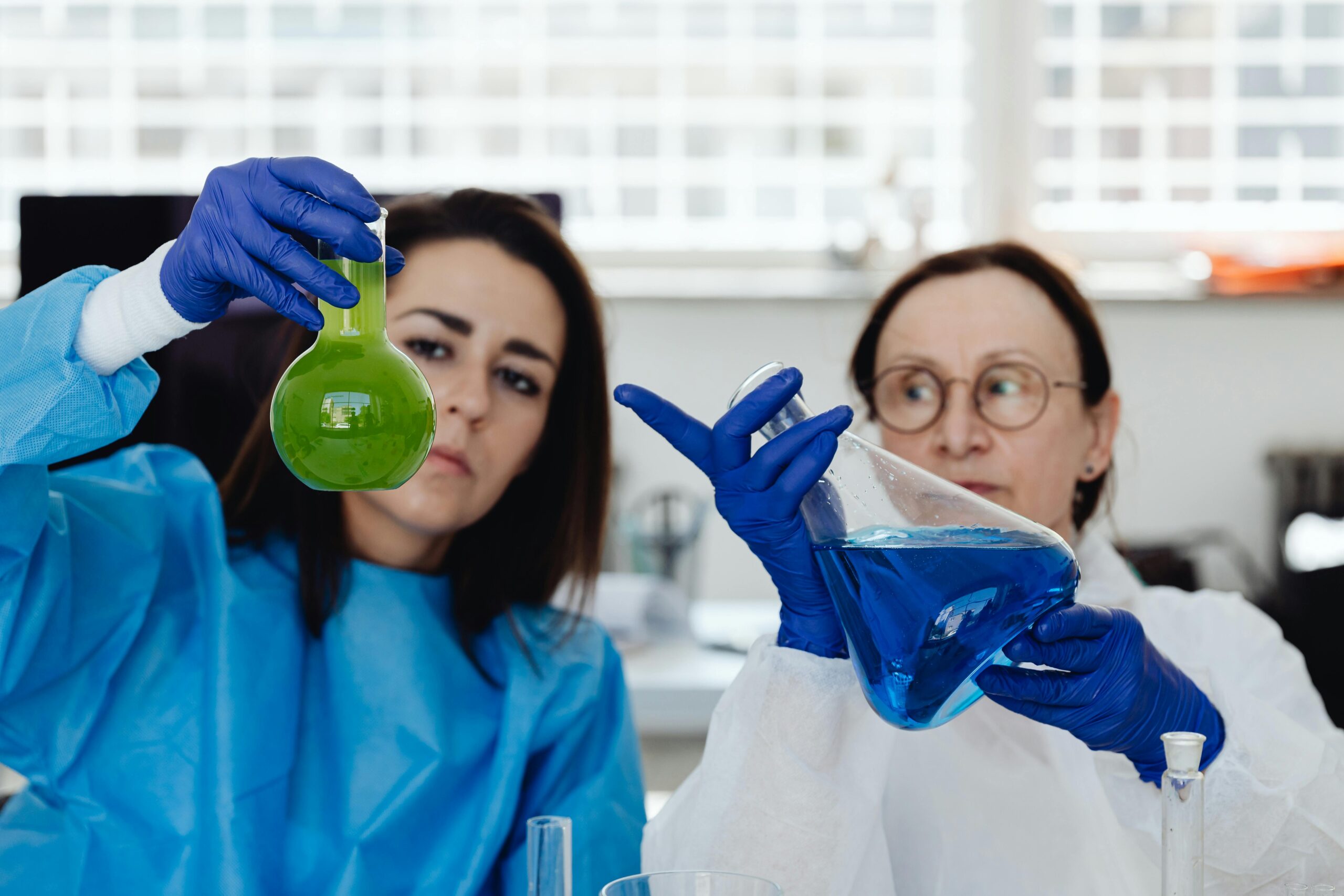 Two female scientists analyze colorful chemical solutions in a laboratory setting.