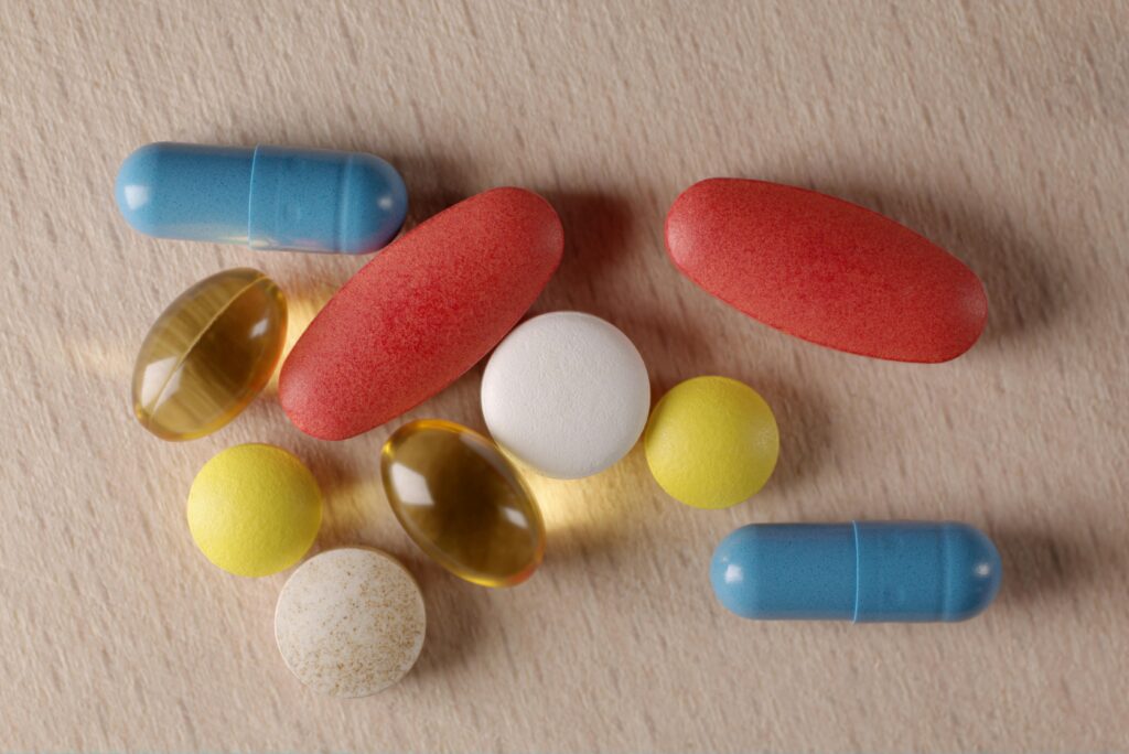 Close-up of various pills and capsules in different colors on a wooden surface.
